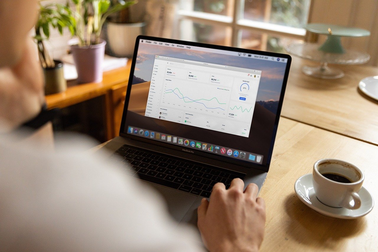 Person working on a laptop showing a line chart, with a cup of coffee